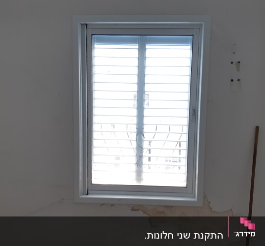 חלון אלומיניום עם תריסים סגורים על קיר לבן